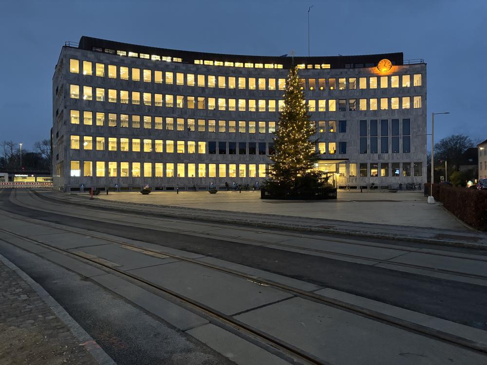 Lyngby Rådhus med letbaneskinner i forgrunden og juletræ med lys på Lyngby Torv. December 2024.