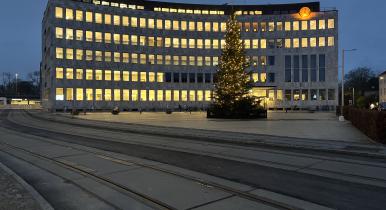 Lyngby Rådhus med letbaneskinner i forgrunden og juletræ med lys på Lyngby Torv. December 2024.